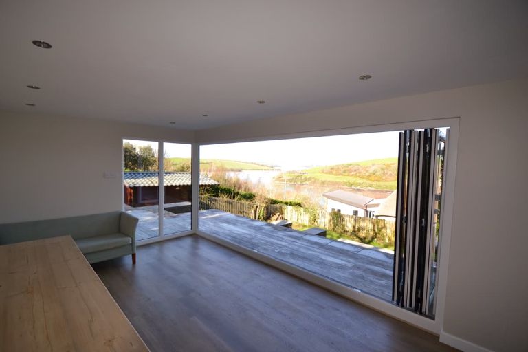 Interior of the garden room looking through the open 5-leaf bi-fold doors to the view of the estuary beyond 