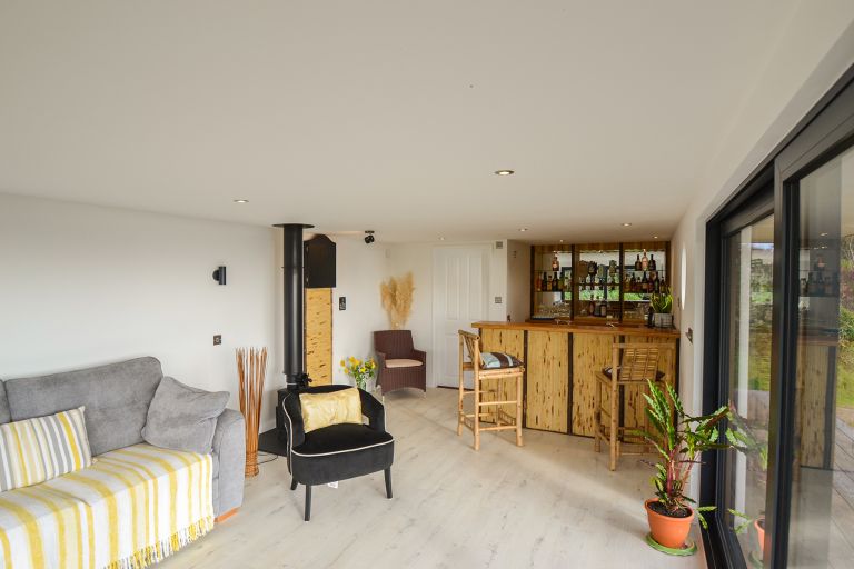 A wide view of the kiki-style garden room. The image shows the bar area, wood-burning stove and sofa