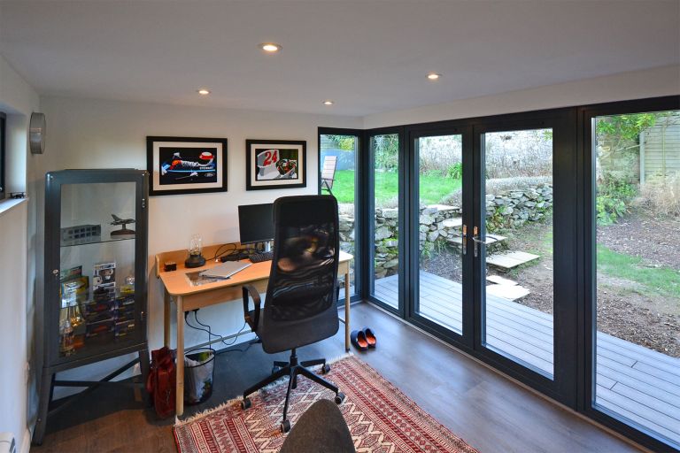 The inside of a Taw Garden Room used as a garden office. Shows the office desk and office chair with large doors to the front and a smaller window for ventilation on the rear elevation