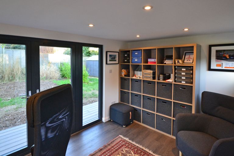 The inside of a Taw Garden Room used as a garden office. A comfy chair for guests and stylish office shelving