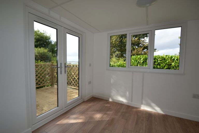 Interior view looking through the double doors. The doors and white internally and grey externally. The decked area, with trellis fencing can be seen through the door